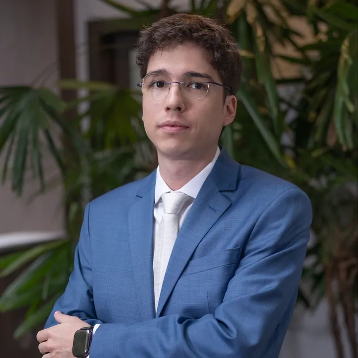 Dr. Vitor Ferrer, cirurgião geral, de terno azul e óculos, com plantas ao fundo